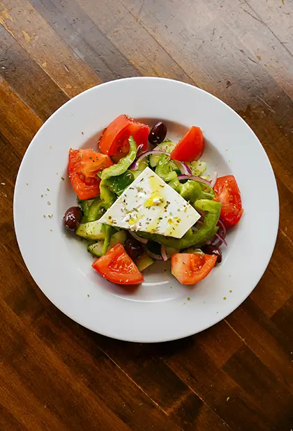 Bowl of Greek salad with colourful veggies on a wooden background