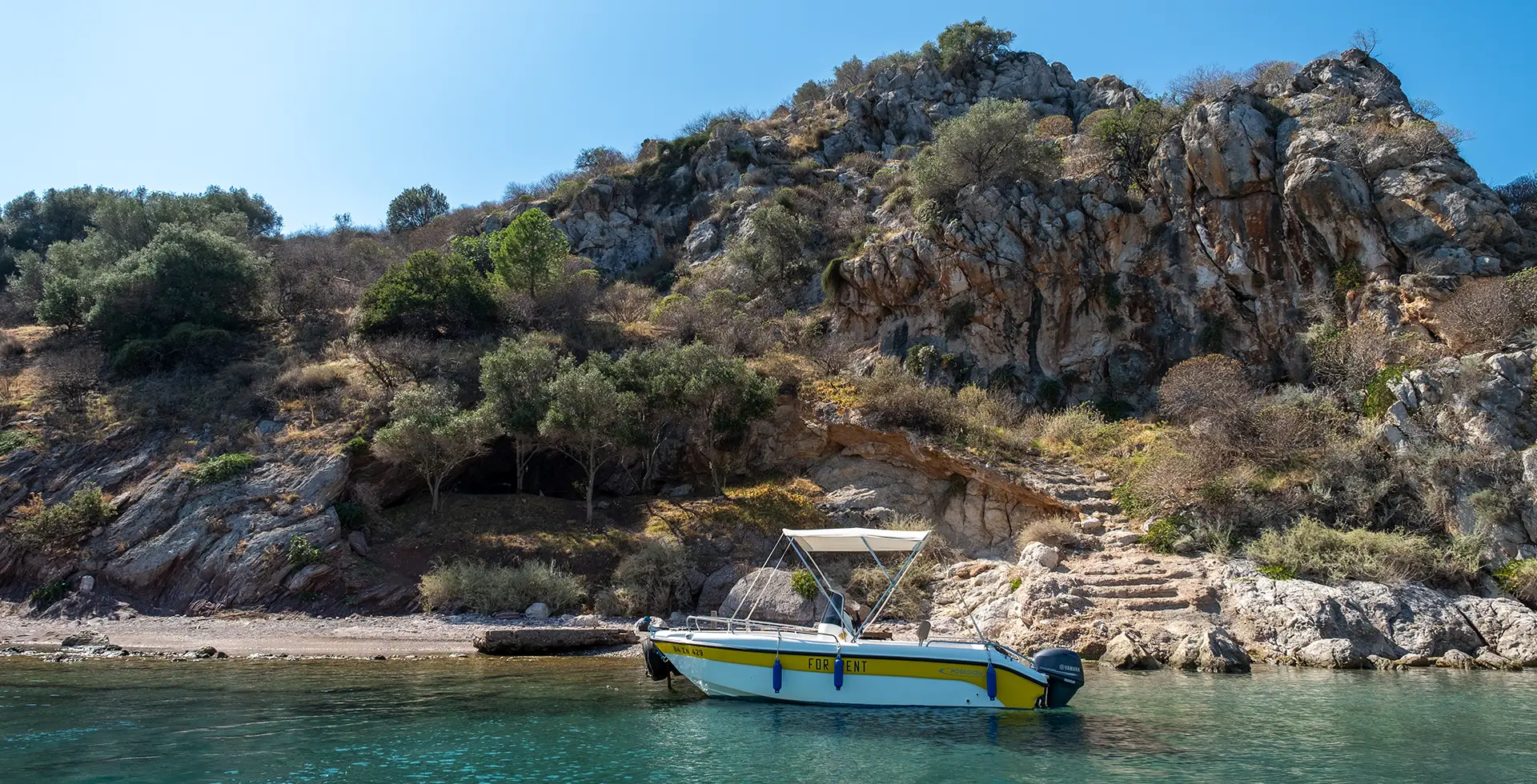 Yellow motorboat anchored on the beach in front of small Tolo island