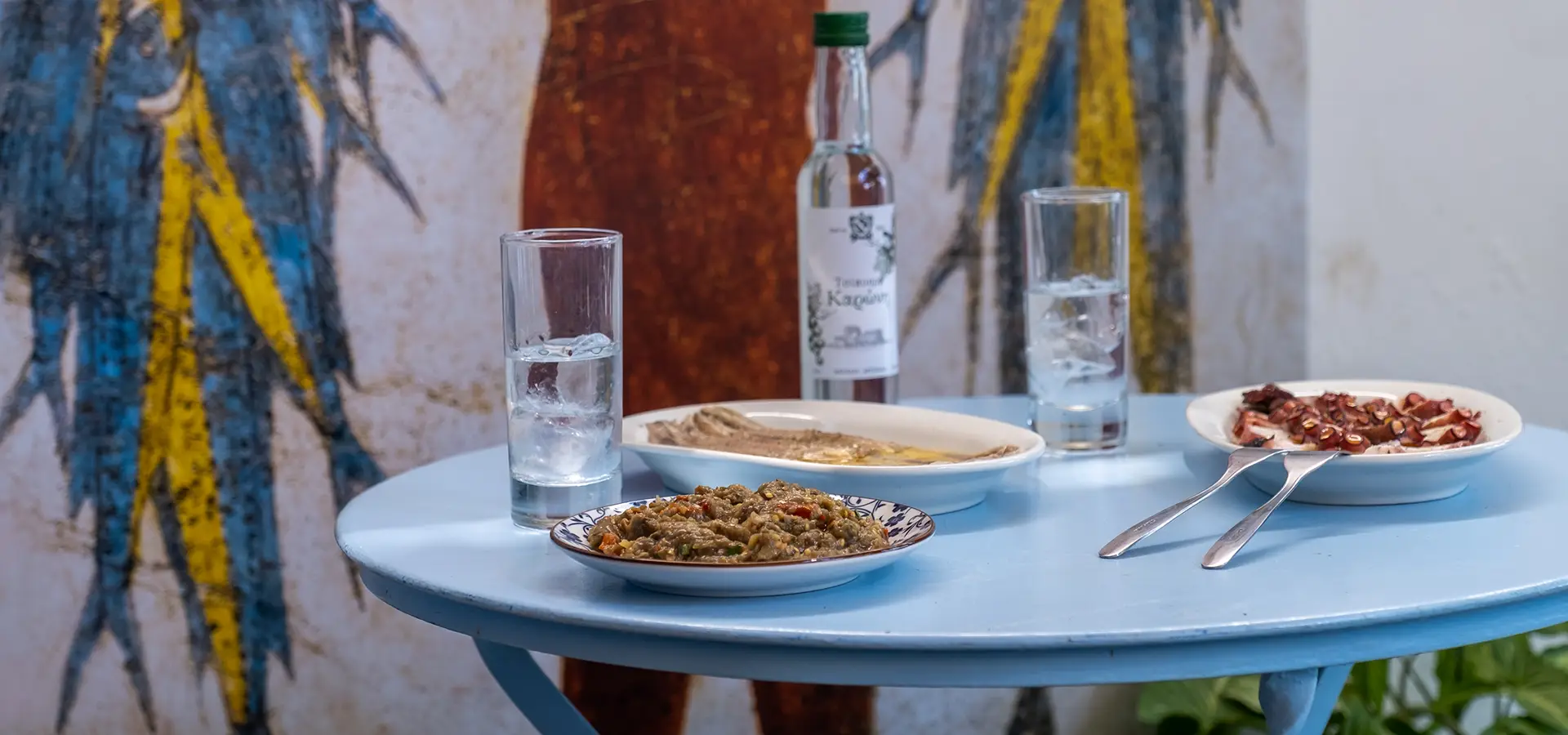 Table of octopus meze in Tolo taverna with a dip and two glasses of tsipouro